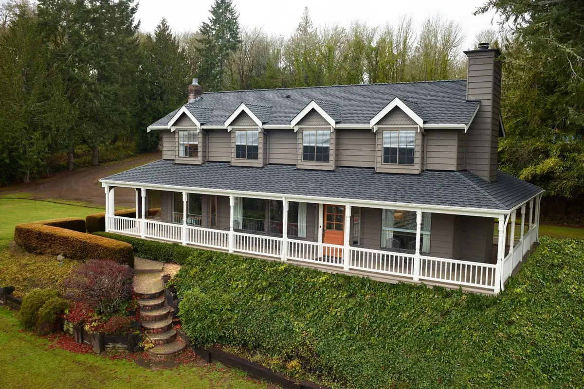 Gray farmhouse with four dormers and a wraparound porch, roofed in GAF Timberline UHDZ Pewter Gray