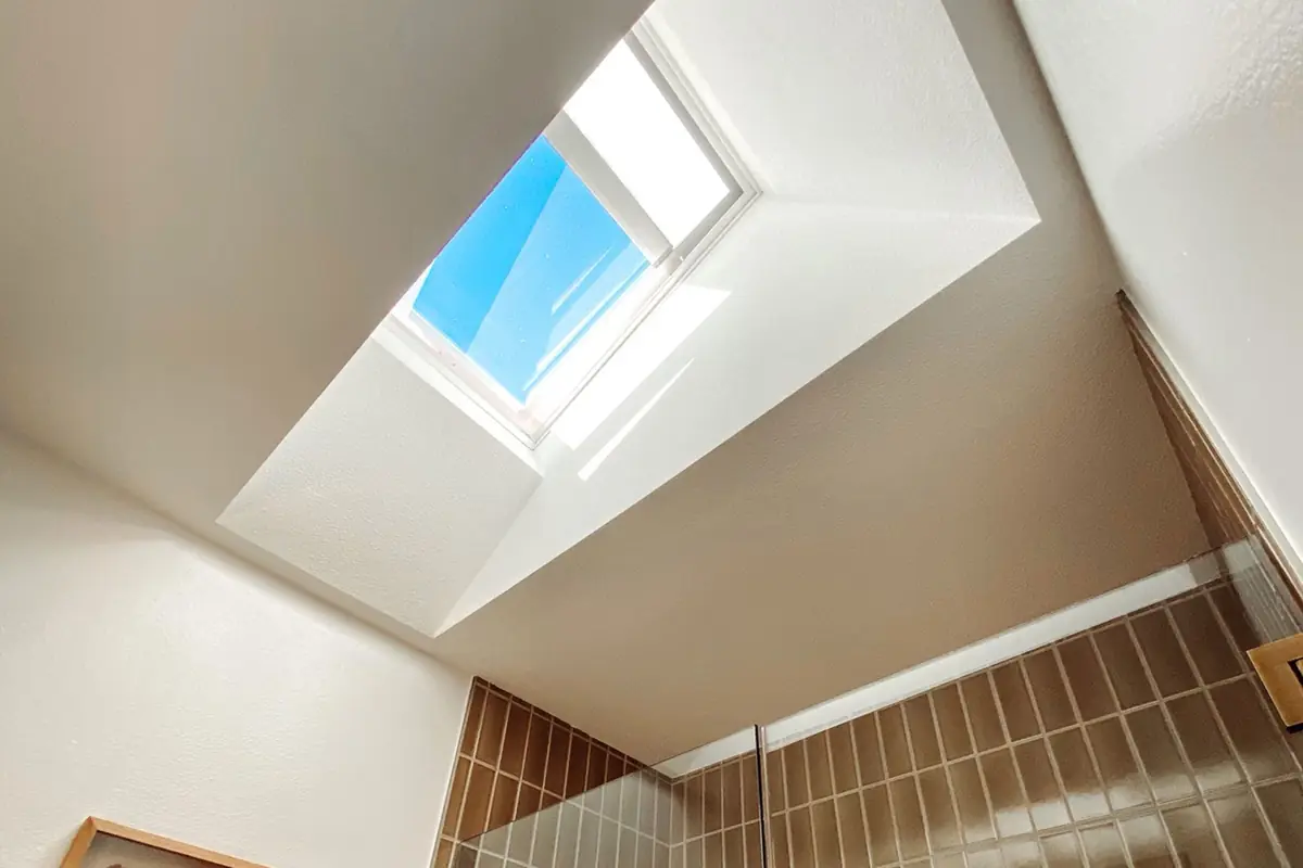 VELUX curb-mount skylight with its shade partly drawn, seen from the bathroom below