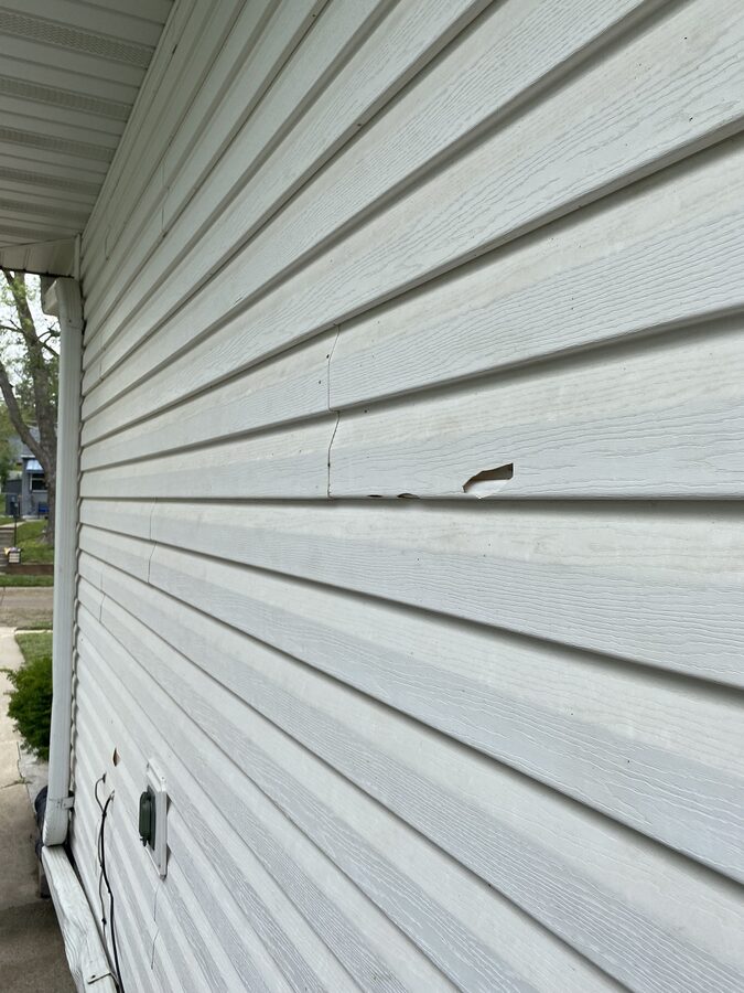 Cracked and broken vinyl siding panel from hail impact