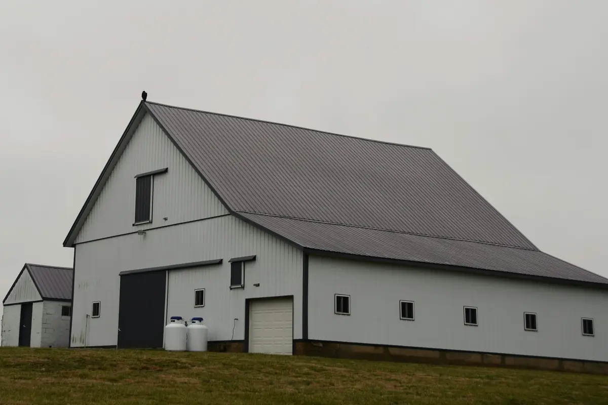 Post-frame barn with a charcoal ribbed metal roof on a grassy rise