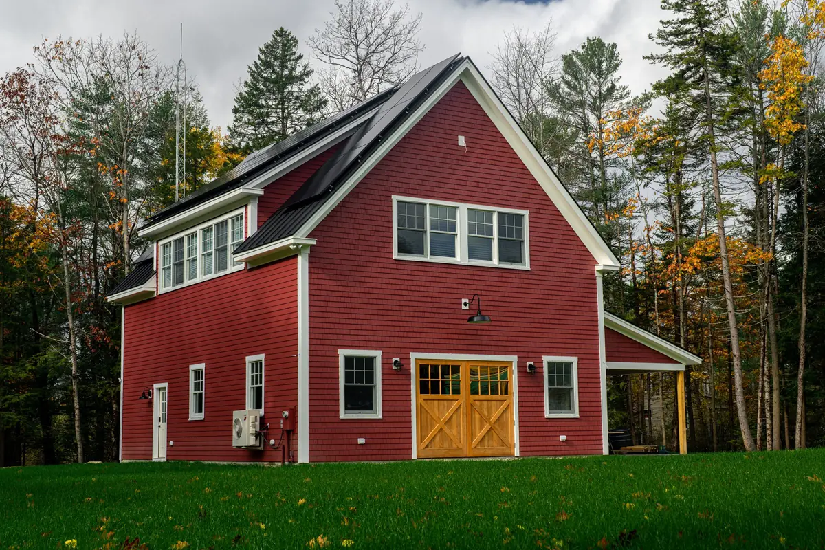 Solar panels mounted on the black standing seam roof of a red carriage house